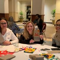 Three women sitting at a table holding decorated lunch bags